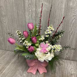 Pink tulips and white flowers arranged in a pink vase with a butterfly decoration.