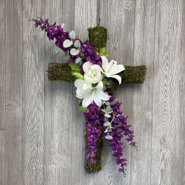 Floral cross with white lilies and purple flowers on a moss-covered cross
