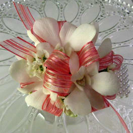 White orchid corsage with pink ribbon on a clear glass plate