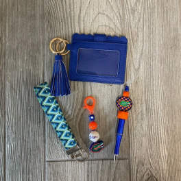 Blue wallet, tassel keychain, patterned strap, and pen on a wood floor