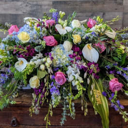 Low elongated arrangement of mixed pink, white, yellow, and blue flowers on a wooden surface