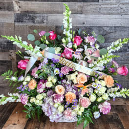 Large pastel sympathy basket with pink roses, snapdragons, and mixed flowers in a white woven basket