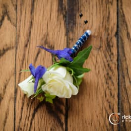 White rose boutonniere with purple accent flowers and a blue wrapped pin