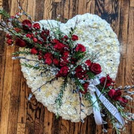 Heart-shaped white funeral arrangement with red rose spray and 'MUMMY' ribbon on a wooden floor