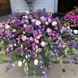 Large cascading arrangement of purple and pink flowers on a low pedestal.