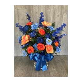Blue and orange floral arrangement in a white vase with a blue ribbon