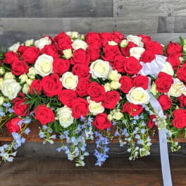 Large red and white rose casket spray with trailing light blue flowers and white ribbon