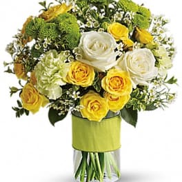 Yellow and white roses arranged in a clear vase with green blooms