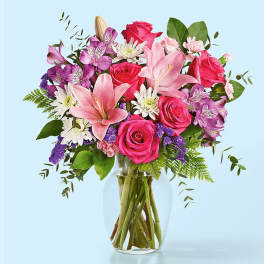Bouquet of pink roses, lilies, and purple flowers in a clear glass vase