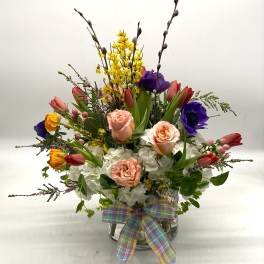Mixed bouquet of roses, tulips, and hydrangeas in a glass vase with a plaid ribbon