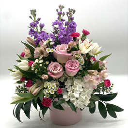 Mixed bouquet of pink roses, purple stock, white hydrangea, and lilies in a pink vase