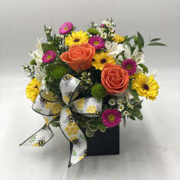 Mixed bouquet with orange roses, yellow daisies, and a bee-patterned ribbon in a black box
