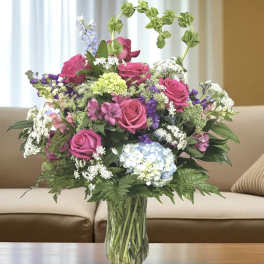 Mixed bouquet of pink roses, hydrangea, and purple flowers in a glass vase