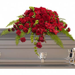 Red rose and carnation casket spray with green accents draped over a gray casket