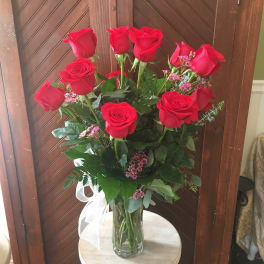Tall vase of red roses with pink filler flowers and a white ribbon