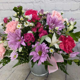 Pink and purple mixed flower arrangement in a metal bucket with a ribbon