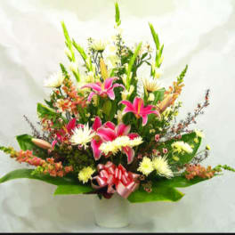 Pink lilies and white daisies in a white vase with a pink ribbon