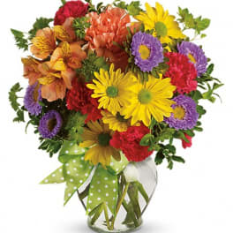 Mixed bouquet of colorful flowers in a clear glass vase with a green polka-dot ribbon