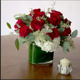 Red roses and white hydrangeas in a glass vase with a small candle beside it