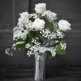 White roses and baby's breath in a silver vase with a cross