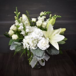 White lilies and roses arranged in a glass vase with silver ribbon