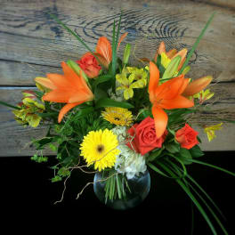 Bouquet of orange lilies, red roses, and yellow daisies in a glass vase