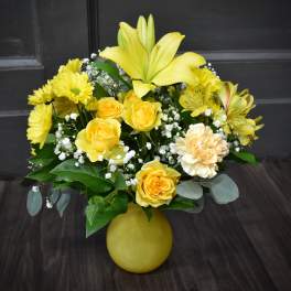 Yellow roses and lilies arranged in a yellow vase