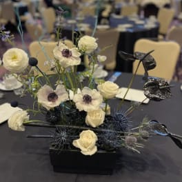 Modern floral centerpiece with white blooms and dark spiky accents in a black vase