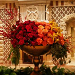 Large arrangement of red, orange, and yellow roses in a pedestal bowl