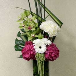 Tall floral arrangement in a glass vase with white roses, orchids, and pink hydrangeas