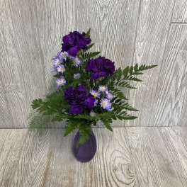 Purple flowers in a small purple vase with fern-like greenery