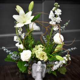 White lilies and roses arranged with greenery in a white angel vase