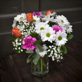 Bouquet of white daisies, orange tulips, and pink carnations in a glass vase