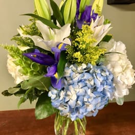 Bouquet of lilies, irises, hydrangeas, and yellow filler in a glass vase