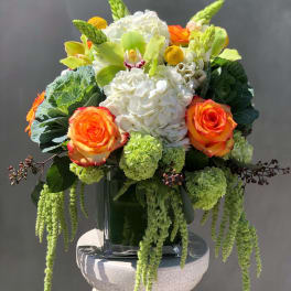 Orange roses and white hydrangeas in a glass vase with trailing green accents
