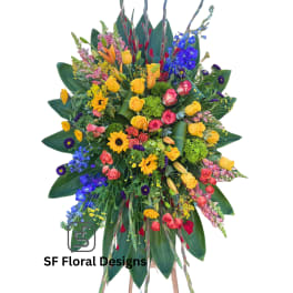 Tall multicolor standing spray with roses, lilies, delphinium, gerbera daisies, and snapdragons on a wooden easel.