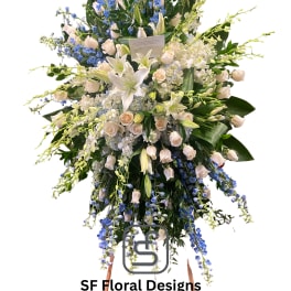 Tall standing spray of white lilies, cream roses, and blue delphinium on a wooden easel