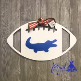 Football-shaped wall sign with a blue alligator silhouette and striped bow