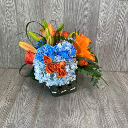 Colorful bouquet with lilies, roses, and hydrangeas in a square container
