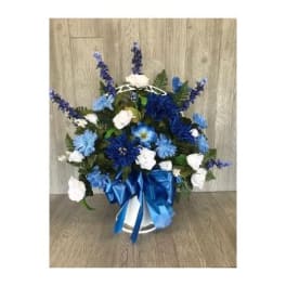 Tall blue and white flower arrangement in a white container with a large blue satin bow
