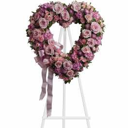 Heart-shaped pink floral wreath on a white easel with ribbon