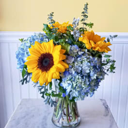 Sunflowers and blue hydrangeas arranged in a clear glass vase
