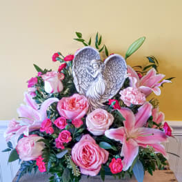 Pink roses and lilies arranged around a heart-shaped angel plaque