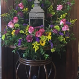 Large floral arrangement with pink roses, purple blooms, and yellow accents around a lantern