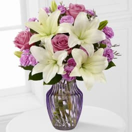 Pink roses and white lilies arranged in a purple glass vase