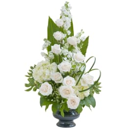 Tall arrangement of white roses, stock, and hydrangeas in a black pedestal vase