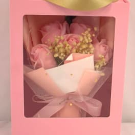 Pink boxed bouquet of pink roses and small yellow filler flowers wrapped in tulle with ribbon