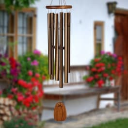 Bronze wind chime hanging outdoors with blurred flowers in the background
