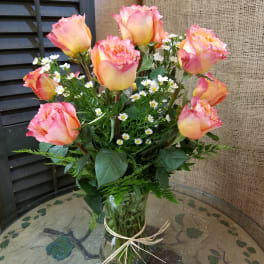 Pink and yellow roses with small white daisies in a glass vase