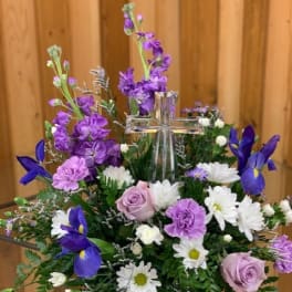 Purple and white floral arrangement with a clear glass cross centerpiece